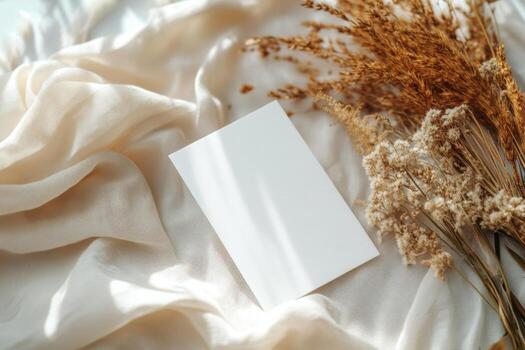 Blank card on soft fabric with dried flowers arranged on a light background in a serene setting photo