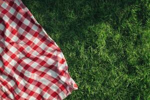 Red and white checkered picnic blanket on lush green grass inviting outdoor relaxation during a sunny day photo