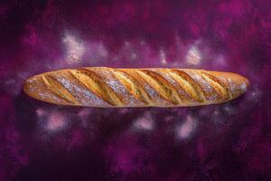 A long, crispy baguette rests on a vibrant purple surface, dusted lightly with flour. The golden crust displays distinct slashes, showcasing its rustic appeal. photo