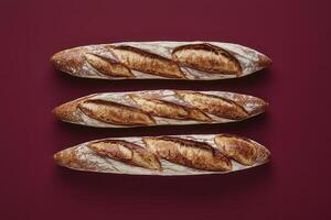 Three golden brown baguettes with crispy crusts are neatly placed on a deep red surface, showcasing their beautiful texture and oven-fresh appearance, evoking a warm bakery atmosphere. photo