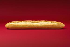 A long, golden bread stick lies flat against a vibrant red backdrop, showcasing its crisp texture and inviting color. The simplicity emphasizes the breads shape and quality. photo