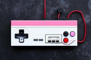 A retro gaming controller features classic buttons and a distinct pink design. It rests on a textured dark surface, showcasing a blend of nostalgia and contemporary style. photo