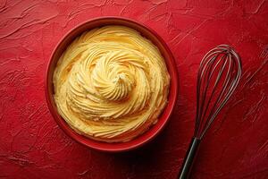 Creamy buttercream frosting is swirled beautifully in a red bowl, accompanied by a metal whisk. This delightful icing is perfect for cakes and cupcakes, adding a rich flavor and texture. photo