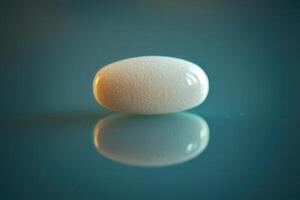 A smooth white capsule rests on a reflective surface, illuminated by soft lighting that enhances its shape. The serene atmosphere emphasizes the simplicity of the subject. photo