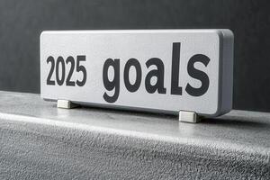 The focus is on a concrete block displaying the text 2025 goals. This setup symbolizes ambition and strategic planning. The minimalist backdrop enhances the theme of future objectives. photo