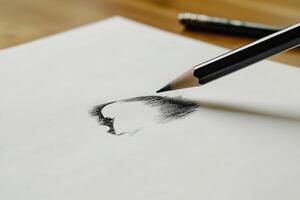 A close-up view of a pencil creating a detailed sketch on white paper. The workspace is simple, highlighting the artistic process in a calm environment. photo