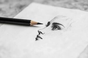 A close-up view of a partial sketch showcasing a womans profile, emphasizing delicate features and expressions. A sharpened black pencil rests next to the artwork, hinting at the artists process. photo