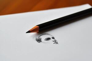 A detailed sketch of a persons profile is positioned on a white sheet of paper. A sharpened pencil rests beside the drawing, highlighting the artistry of sketching. photo