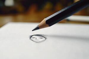 A pencil hovers just above a newly drawn face sketch on white paper. Soft lighting enhances the details of the artwork. The artists focus is evident in the subtle shadows. photo