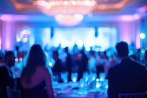 Guests sit at elegantly arranged tables in a beautifully lit venue, enjoying dinner and entertainment during a lively evening banquet. The ambiance is enhanced by colorful lighting and decorations. photo