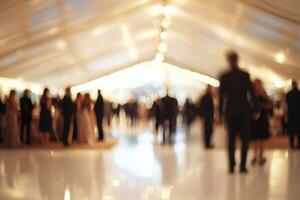 Guests dressed in formal attire engage in conversation at an elegant evening gala held in a beautifully lit tent. The atmosphere is lively, creating a festive mood for the celebration. photo