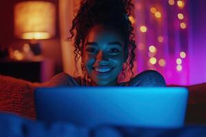 A young woman smiles brightly while using a laptop in a warm, dimly lit room adorned with string lights. The relaxed atmosphere enhances her joyful expression during her evening activity. photo