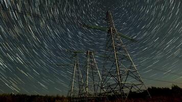 Witness the mesmerizing movement of stars forming trails against a dark sky, set above towering power lines. The captivating view showcases the beauty of nature and technology together. video