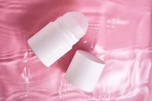 Roll-on deodorant on a pink background in water. photo