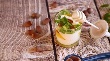 homemade yogurt with kiwi, honey and nuts in a glass on a wooden table video