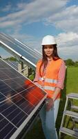 Portrait of professional woman engineer in uniform with tools looking at camera in solar power station. Vertical video