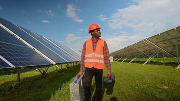 African American energy engineer in uniform checking solar panels while walking on field video