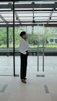 Panoramic view from skyscraper building. Businesswoman standing near window in new modern office and talking by smartphone. Communication, management and productive work concept. Vertical shot video