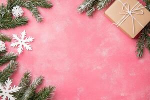 Festive pine garland and gift on pink background with snowflakes photo