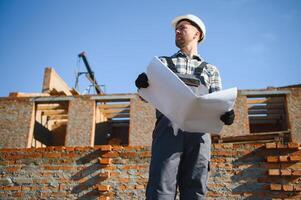 An architect or engineer on the construction of brick houses holds the construction plan in his hands and checks the execution of the work photo