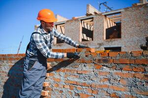 Bricklayer industrial worker installing brick masonry on exterior wall with trowel putty knife photo