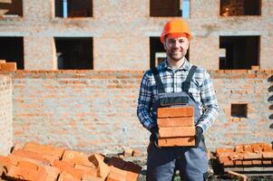 Young adult man builder working at object carrying bricks at construction site photo