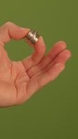 A closeup view of a hand elegantly holding a shimmering silver ring set against a green background video