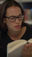 A young woman looks confused while deeply engrossed in reading a book in a library video