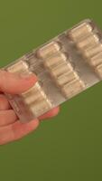A hand is holding a blister pack that contains pills set against a vibrant green background video