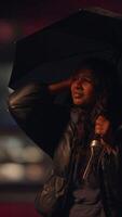 A woman stands in the rain holding an umbrella while using a microphone for her performance video