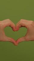 Hands Gently Forming a Heart Shape Against a Bright and Inviting Green Background video