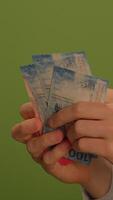 A closeup view of a human hand firmly grasping a torn and damaged banknote in display video