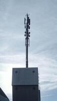 A telecommunications tower stands tall against a backdrop of moving cloudy skies above video