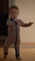 A joyful toddler dressed in colorful pajamas is happily walking around indoors, exploring video