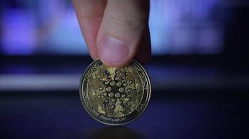 A person is holding a cryptocurrency coin against a backdrop of a digital environment video