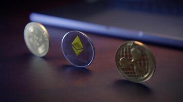 A collection of various Cryptocurrency coins displayed on a desk near a laptop device video