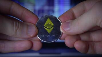 A Hand Holding an Ethereum Coin Set Against a Background of Digital Investment Strategy and Concepts video