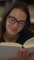 A Woman Happily Engaged in Reading a Book Inside a Library Surrounded by Bookshelves video