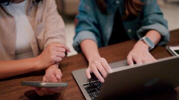 Collaborative Focus. Two colleagues work side-by-side at a wooden table, one engrossed in their laptop while the other checks their phone. video