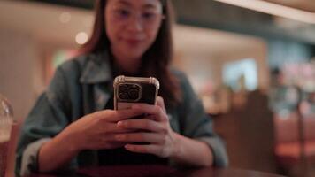 Woman Using Smartphone in Cafe. A young woman scrolls through her phone, lost in the digital world, while enjoying a cup of coffee in a cozy cafe. The image captures the casual. video