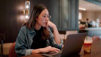 Focused Concentration.A young woman working on her laptop in a modern coffee shop, thoughtfully navigating her day's tasks, showcasing the essence of focus and determination. video