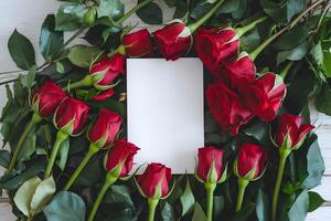 A blank white greeting card is surrounded by bunch of red roses representing concepts like Valentines Day or any such occasions photo