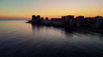 Warm golden light enveloping mersin's coastline, casting elongated shadows from urban structures onto serene mediterranean waters during twilight hours video