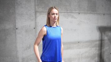 A woman in a blue tank top works out in a gym with dumbbells, showing determination in fitness video