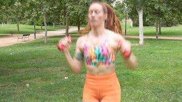 A woman in a park, working out with dumbbells, shows determination in her fitness routine video