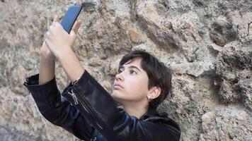 A young urban individual is joyfully capturing a selfie while against a textured wall backdrop video