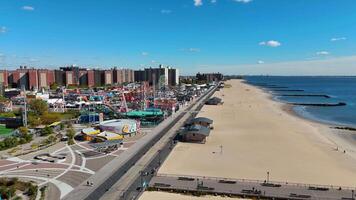 Aerial view of beachfront with amusement park and boardwalk - A vibrant aerial view showcasing a sandy beach, a bustling amusement park, a boardwalk, and coastal waters under a clear blue sky. video