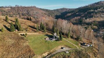 Hillside A-Frame Cabin with Scenic Views. Aerial view of an A-frame cabin on a grassy hillside, surrounded by trees and rolling hills under a clear blue sky. video