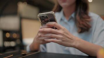 Woman texting on phone in cafe. Close-up shot of a woman's hands using a smartphone, showcasing a modern, minimalist style, with a blurred background of a cafe setting. video