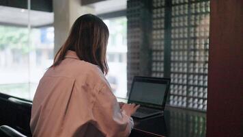A woman is working on a laptop in a coffee shop, with her shadow cast from behind a window. This image shows determination and focus. video